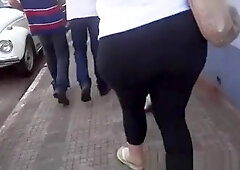Large chubby butt woman in ebony leggings and white t-shirt walking on the street.