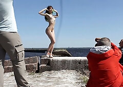 Woman poses nude on a weathered concrete pier during an outdoor photo session