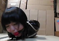 Japanese beauty in black latex catsuit bound in shibari rope in a dim warehouse