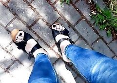 a crossdresser with very hot feet in broad daylight walks in public in a park in taut jeans and very high wedge heels
